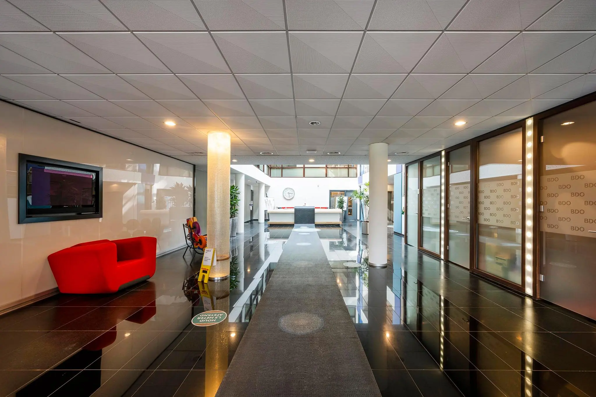 Moderne entreehal van een kantoorpand aan de K.P. van der Mandelelaan met strakke inrichting, glazen wanden en een receptiebalie.